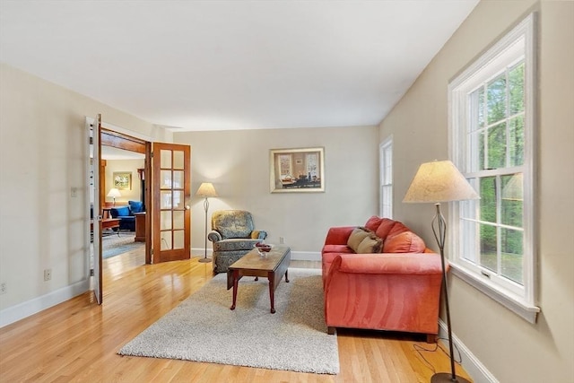 sitting room with french doors, healthy amount of natural light, light wood-style floors, and baseboards