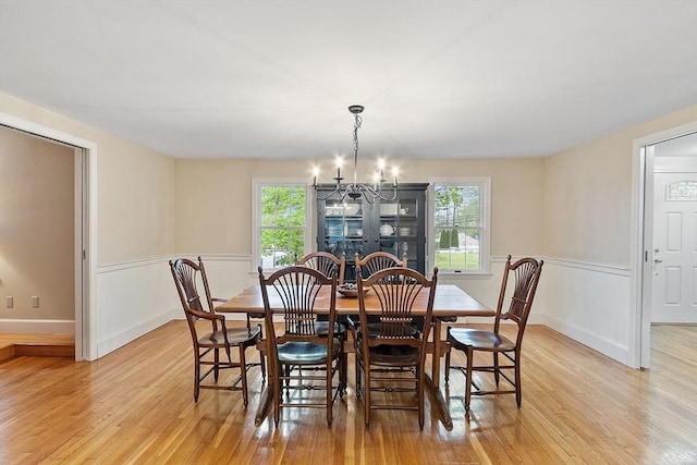 dining area with light wood finished floors, a chandelier, plenty of natural light, and a wainscoted wall