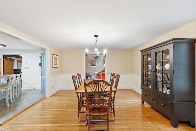 dining area featuring a chandelier, light wood-type flooring, and wainscoting