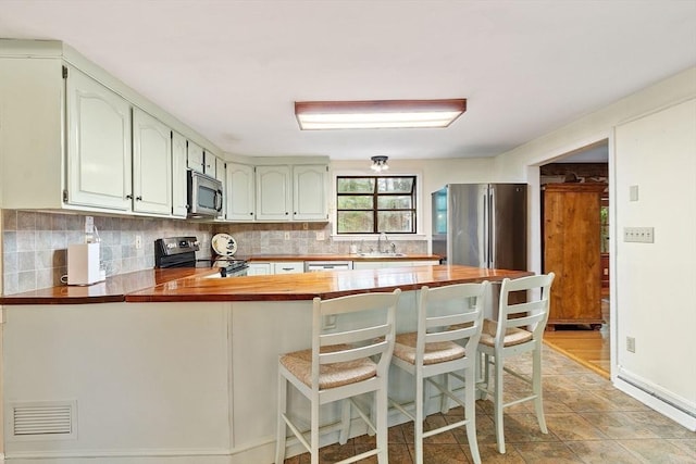 kitchen with appliances with stainless steel finishes, a peninsula, tasteful backsplash, and wood counters