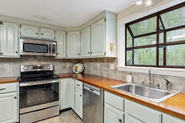 kitchen featuring stainless steel appliances, a sink, butcher block counters, light tile patterned floors, and backsplash