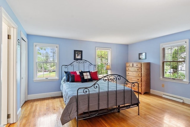 bedroom with a baseboard radiator, light wood finished floors, and multiple windows
