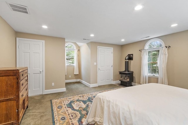 carpeted bedroom featuring multiple windows, baseboards, recessed lighting, and a wood stove