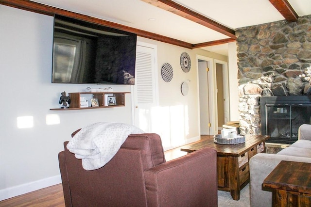 living room featuring a stone fireplace, beamed ceiling, and wood-type flooring