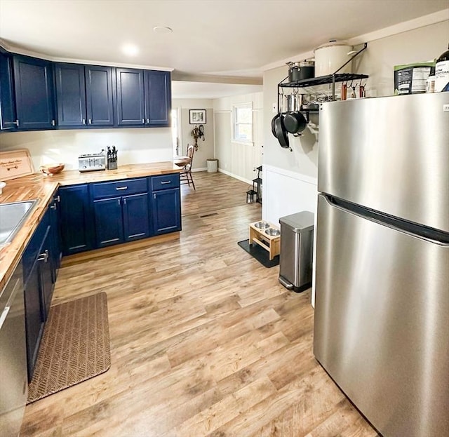 kitchen featuring butcher block countertops, light wood-type flooring, blue cabinetry, and appliances with stainless steel finishes