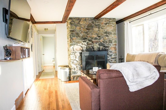 living room with a fireplace, beam ceiling, and light wood-type flooring