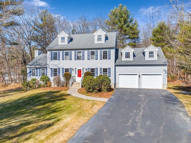 colonial-style house featuring driveway, an attached garage, a front lawn, and a shingled roof