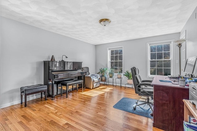 office area with light wood finished floors, a textured ceiling, and baseboards