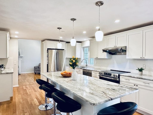 kitchen featuring a breakfast bar area, light wood-style flooring, appliances with stainless steel finishes, under cabinet range hood, and white cabinetry