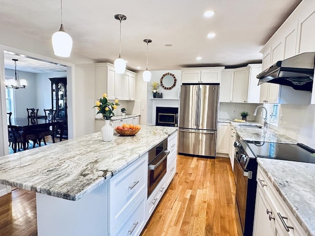 kitchen featuring a sink, under cabinet range hood, appliances with stainless steel finishes, white cabinetry, and light wood-type flooring