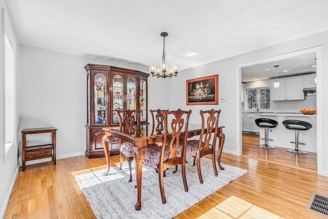 dining space featuring visible vents, baseboards, a chandelier, and light wood finished floors