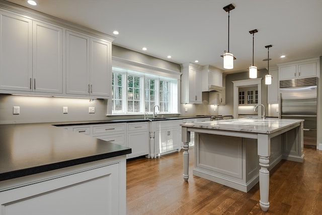 kitchen featuring a kitchen breakfast bar, decorative light fixtures, built in refrigerator, dark hardwood / wood-style flooring, and sink