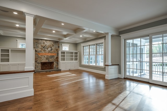 unfurnished living room featuring hardwood / wood-style floors, beam ceiling, coffered ceiling, a stone fireplace, and ornate columns