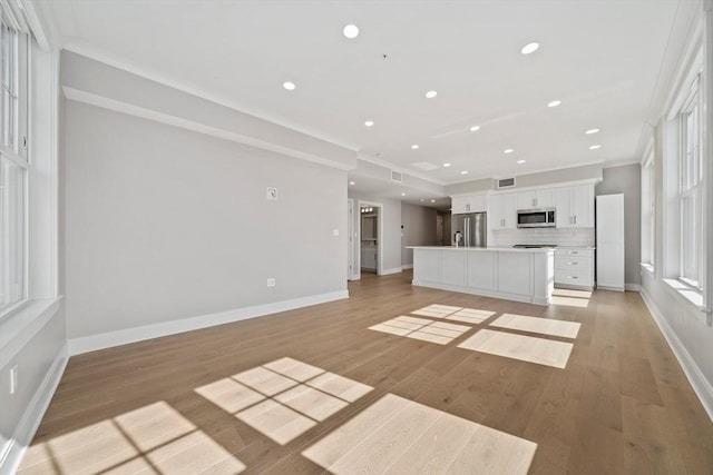 unfurnished living room with crown molding, recessed lighting, baseboards, and light wood-type flooring