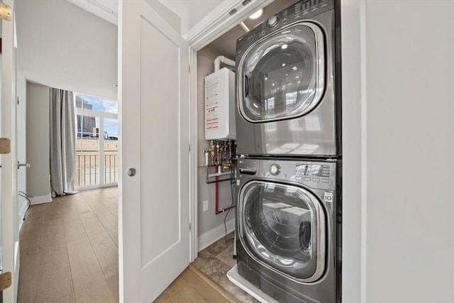 laundry room featuring laundry area, wood finished floors, stacked washer / drying machine, and baseboards