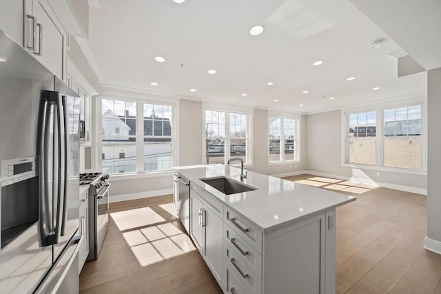 kitchen with light stone counters, wood finished floors, a sink, ornamental molding, and stainless steel appliances