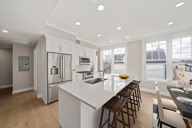 kitchen with visible vents, a kitchen island with sink, a sink, stainless steel appliances, and tasteful backsplash