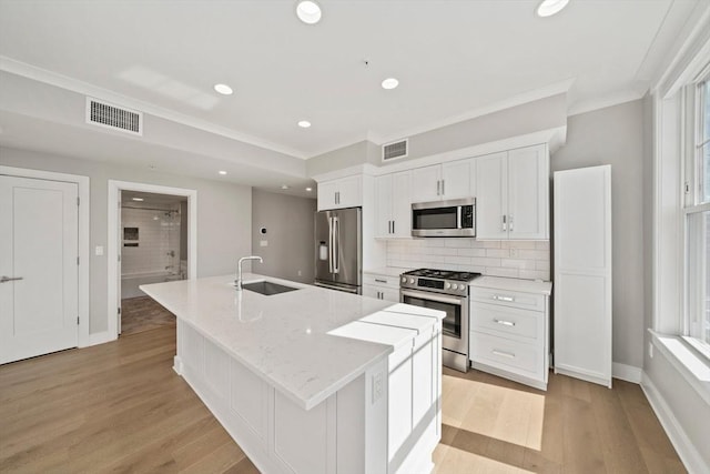 kitchen with visible vents, a sink, white cabinets, stainless steel appliances, and a kitchen island with sink