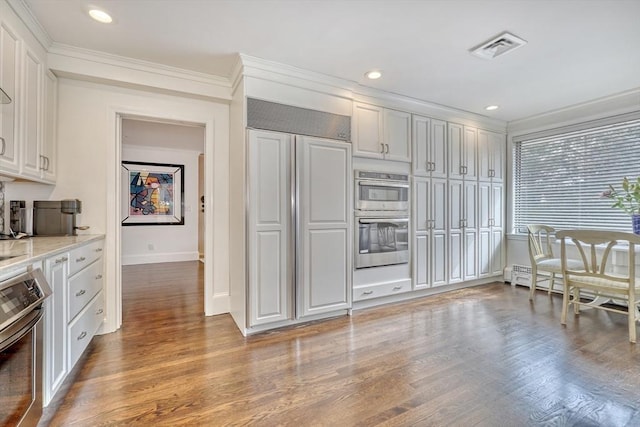 kitchen with stainless steel double oven, wood finished floors, visible vents, and paneled built in refrigerator