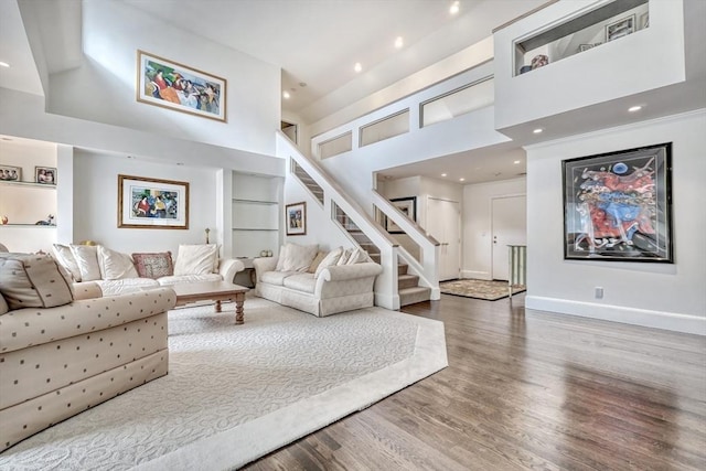 living room featuring recessed lighting, a towering ceiling, wood finished floors, baseboards, and stairs