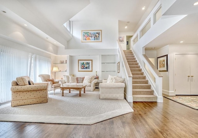 living area with stairs, recessed lighting, a high ceiling, and wood finished floors