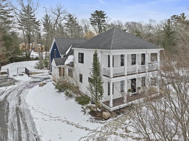 view of snowy exterior with a shingled roof and a balcony