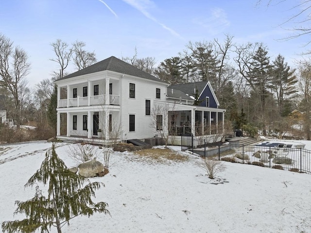 snow covered property with a balcony, a sunroom, and fence