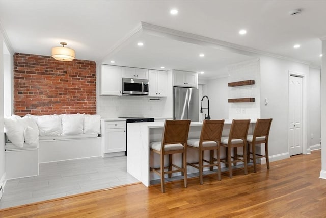 117 Fulton St Unit 4, Boston, MA 02109 - kitchen featuring appliances with stainless steel finishes, crown molding, light wood-style floors, white cabinets, and a breakfast bar area