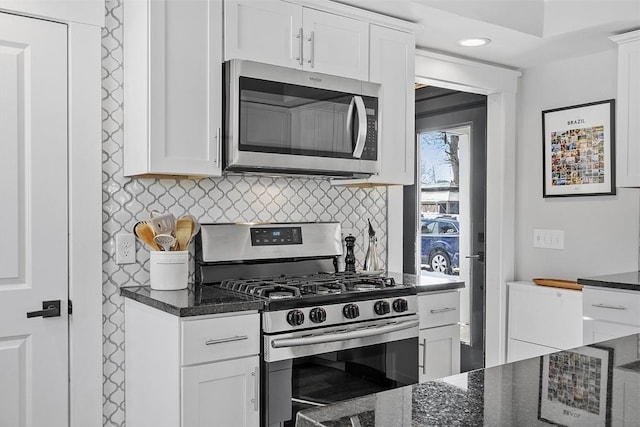 kitchen featuring dark stone counters, stainless steel appliances, white cabinetry, and decorative backsplash