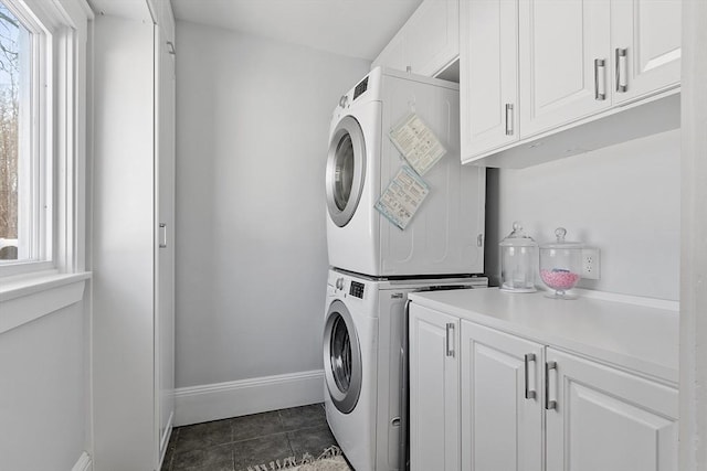 laundry room with cabinets, dark tile patterned flooring, and stacked washer / drying machine