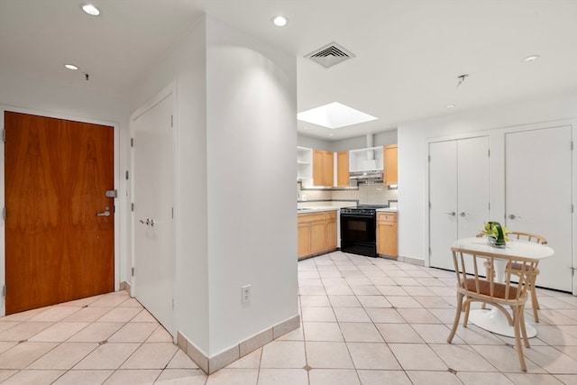 kitchen with light brown cabinets, black range oven, a skylight, light tile patterned floors, and backsplash