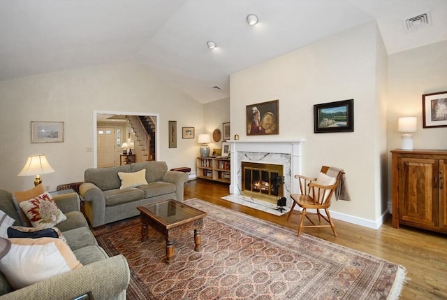 living area with lofted ceiling, visible vents, a premium fireplace, wood finished floors, and stairs