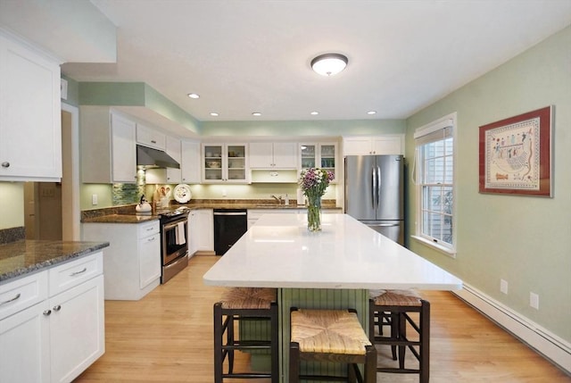 kitchen with a baseboard radiator, appliances with stainless steel finishes, a kitchen breakfast bar, under cabinet range hood, and a sink