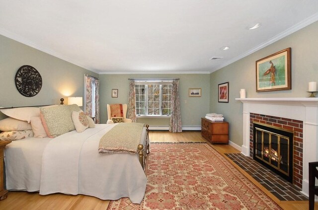 bedroom with a brick fireplace, wood finished floors, and crown molding