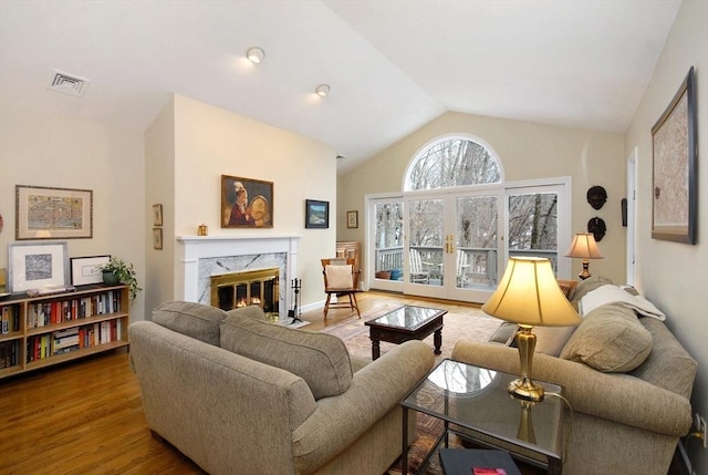 living area featuring visible vents, lofted ceiling, a premium fireplace, wood finished floors, and french doors