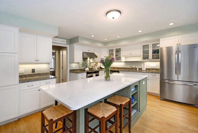 kitchen featuring a breakfast bar area, stainless steel appliances, light wood-style flooring, white cabinetry, and under cabinet range hood