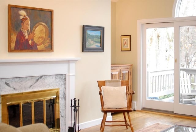 living area with a high end fireplace, a healthy amount of sunlight, baseboards, and wood finished floors