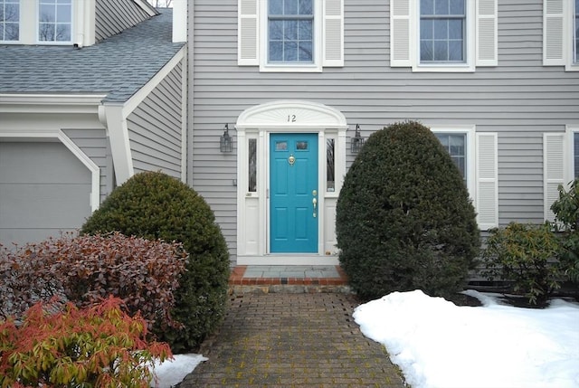 doorway to property with a garage and a shingled roof