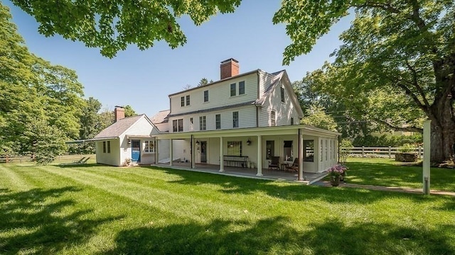 back of property with a lawn, a chimney, and fence