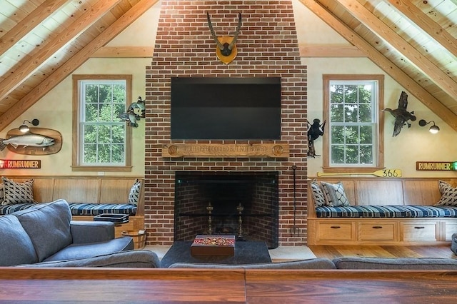 living area with vaulted ceiling with beams, wood ceiling, a healthy amount of sunlight, a wainscoted wall, and a fireplace