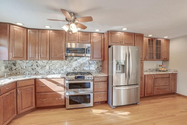 kitchen with sink, light stone counters, tasteful backsplash, stainless steel appliances, and light hardwood / wood-style floors