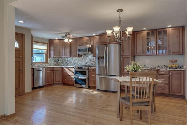 kitchen with pendant lighting, backsplash, light stone counters, light hardwood / wood-style floors, and stainless steel appliances