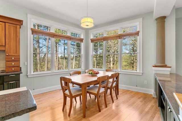 dining room featuring light wood-type flooring, plenty of natural light, baseboards, and ornate columns