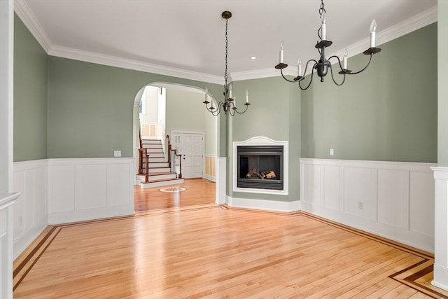 unfurnished living room with wood finished floors, ornamental molding, and a notable chandelier