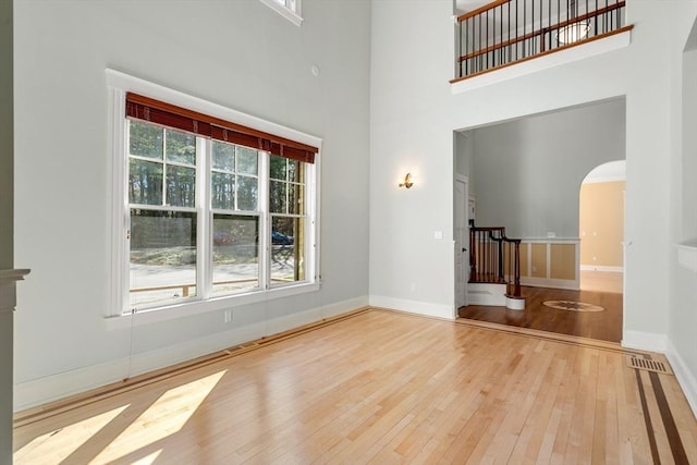 unfurnished living room with hardwood / wood-style flooring, visible vents, arched walkways, a high ceiling, and baseboards