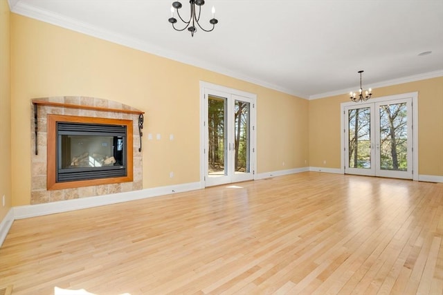 unfurnished living room featuring ornamental molding, baseboards, a notable chandelier, a glass covered fireplace, and light wood-style floors