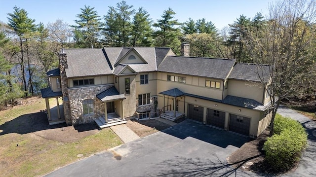 view of front of property with a chimney, driveway, stone siding, and a garage
