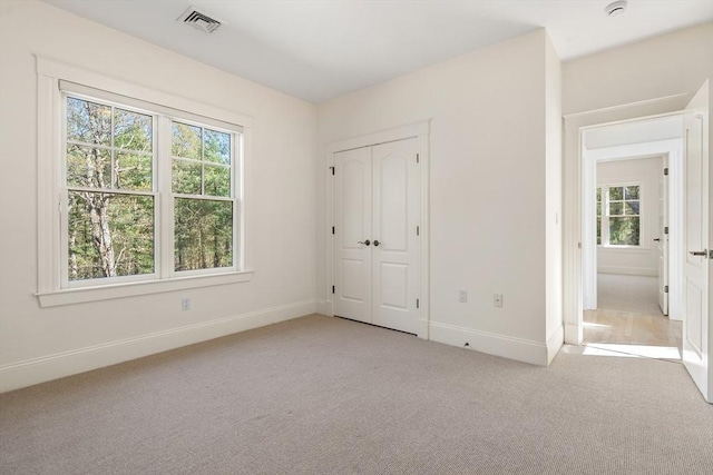 unfurnished bedroom with multiple windows, visible vents, baseboards, and light carpet