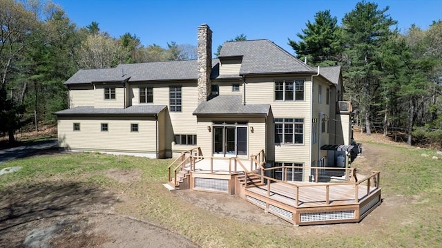 rear view of house featuring a chimney, a deck, and a lawn