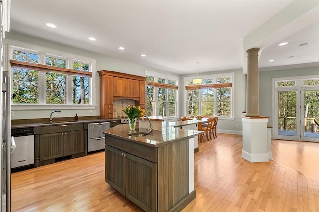 kitchen with stainless steel dishwasher, light wood-style flooring, decorative columns, and a sink